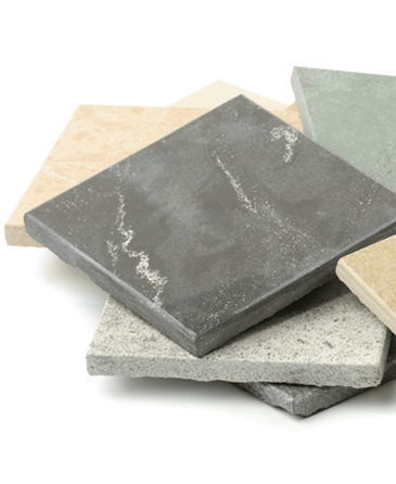 A stack of assorted square stone tiles in various shades, including gray, beige, and green. The surfaces are textured, conveying a natural, earthy feel.